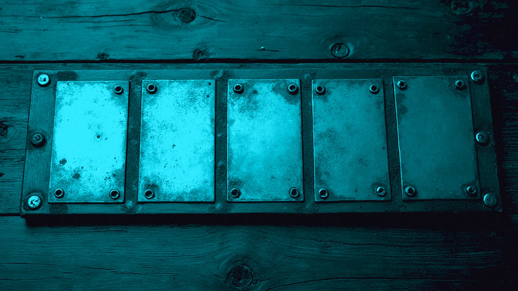 A metal strip under cyan stage light, cut into five plates; the first three sit slightly closer together than the last two.