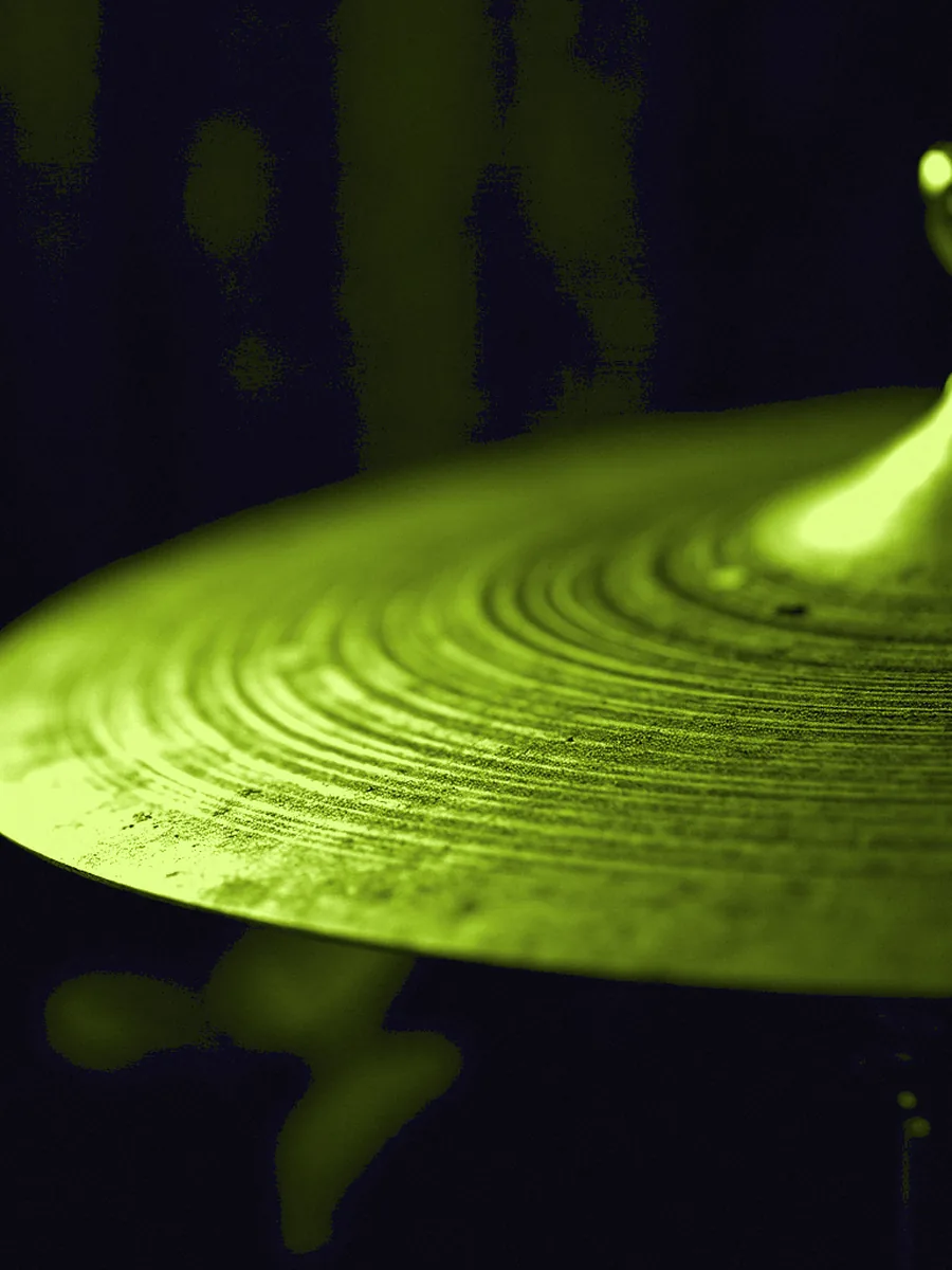 Two thin cymbals closed edge to edge under a lime gel, the lathe rings running across the bronze